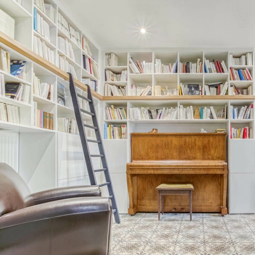 Bibliothèque sur mesure en angle avec échelle grise réalisée à Lausanne dans une pièce avec un piano