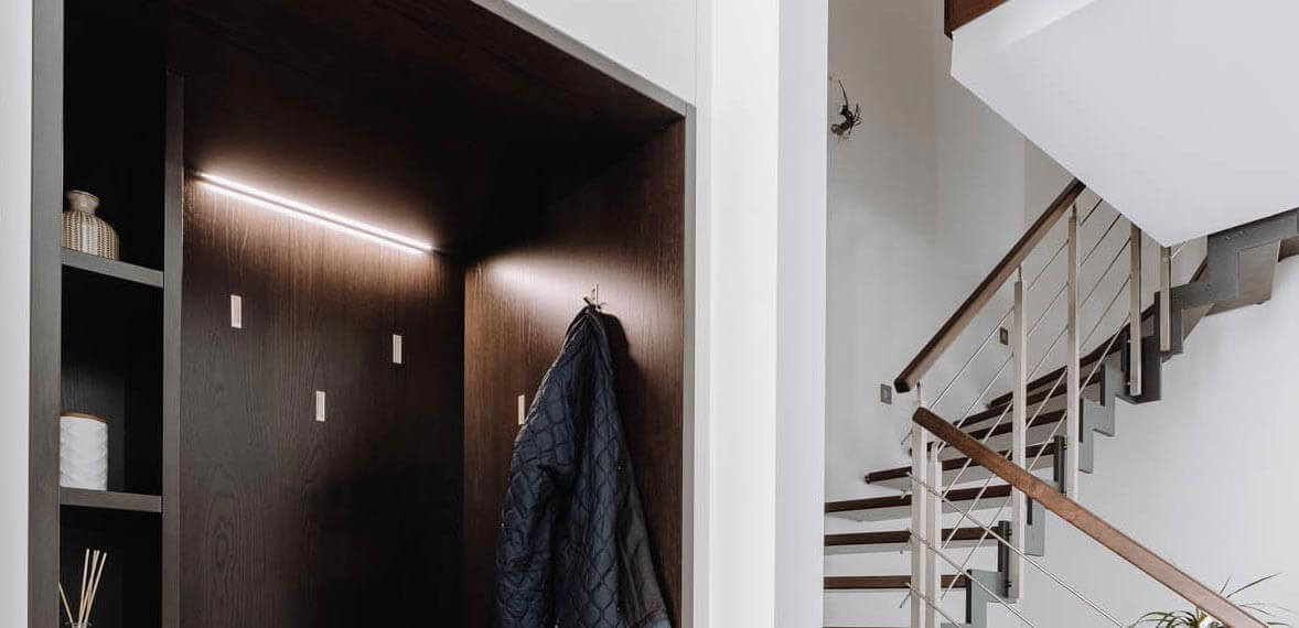 Aménagement d'une entrée de Maison près de Paris avec un meuble placard blanc et niche bois sombre et éclairage