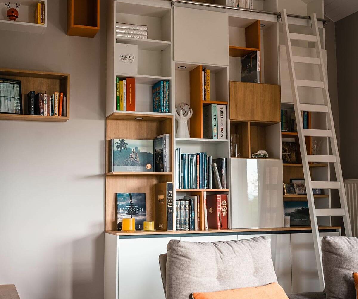 Bibliothèque sur-mesure colorée sous pente avec échelle, pour une ambiance cosy et chaleureuse.